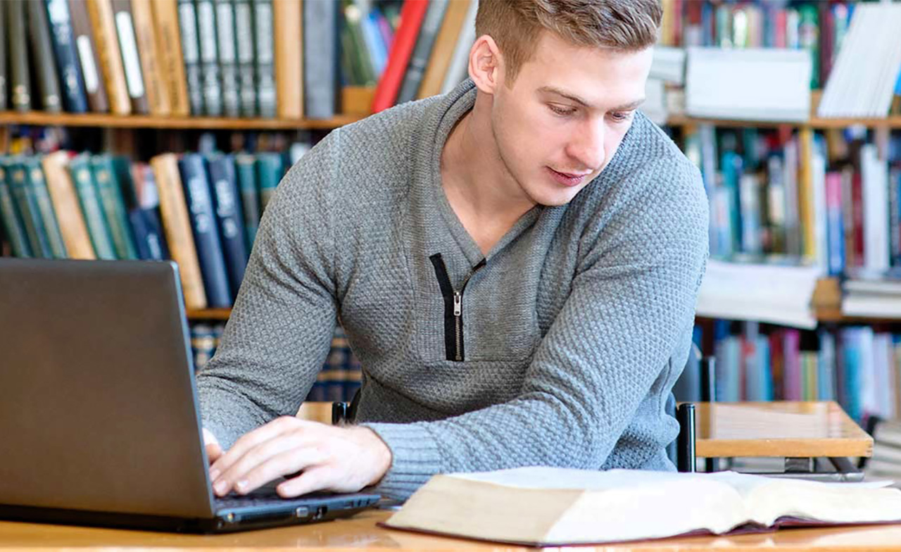 Young male student typing on laptop in the university library